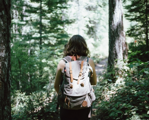 girl with brown hair walking through the woods with a backpack on
